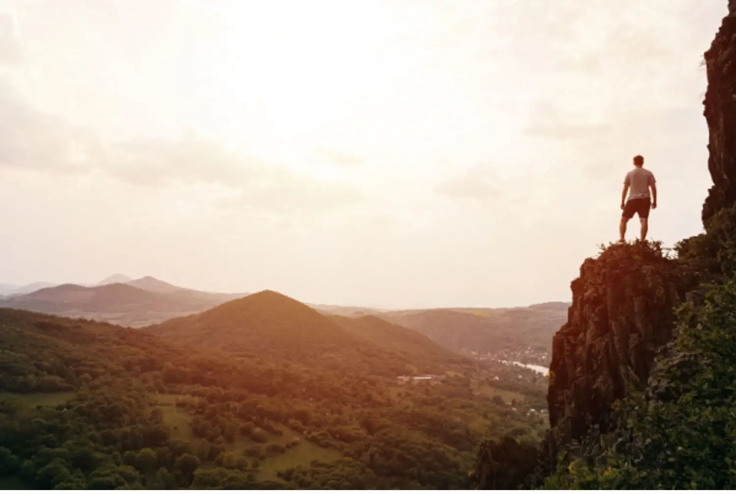 Proud man standing on a cliffside overlooking a scenic view of valleys and mountains